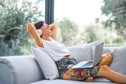 Woman Sitting on Couch While Smiling with Headphones and Laptop